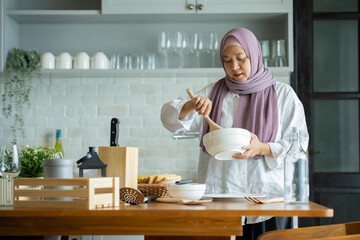 Wall Mural - A Muslim woman is preparing to cook breakfast for her family. At the beautiful kitchen in her house, having fun woman with hijab preparing dinner, Islamic woman Enjoying Doing Homemade.