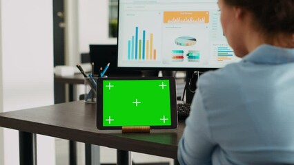 Company employee having tablet on desk with greenscreen display in startup agency office, using blank mockup template and isolated chromakey layout. Woman looking at digital web app on device.