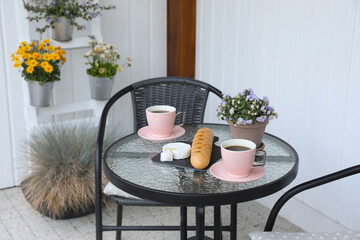 Canvas Print - Cups of coffee, potted plant, bread and cheese on glass table. Relaxing place at outdoor terrace