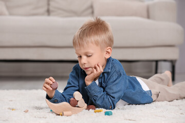 Sticker - Cute little boy playing with wooden balance toy on carpet indoors