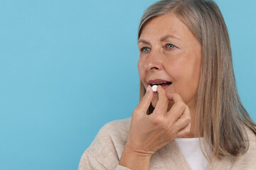 Sticker - Senior woman taking pill on light blue background. Space for text