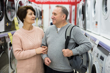 Wall Mural - Happy spouses of mature age, who came to the electronics and household appliances store for shopping, choose a washing ..machine