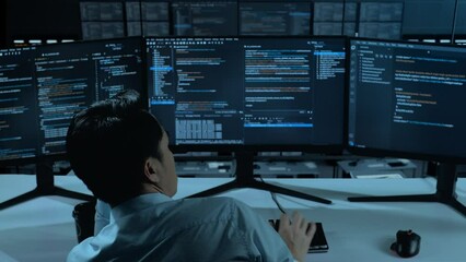 Back View Of Bored Asian Man Developer Write Code With Multiple Computer Screens In The Office
