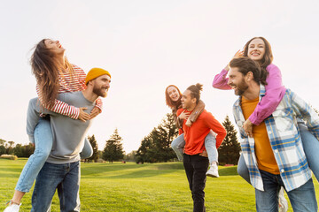 Wall Mural - Group of smiling multiracial friends, women and men carry on shoulders, having fun in green park. Diversity, friendship, meeting concept 