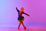 Beautiful, adorable little girl, child in stage costume dancing, performing figure skating against gradient pink purple background in neon. Concept of childhood, figure skating sport, hobby, school