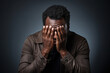 © Tatyana - Portrait of an exhausted man of African nationality covering his face with his hands, in a brown shirt on a gray studio background, failure, fatigue, difficult to choose. Professional burnout concept.