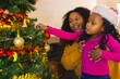 © Wavebreak Media - Happy african american mother and daughter decorating christmas tree at home, copy space