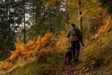 Fototapeta  - game warden hiking through forest with German shorthaired pointer on the hunt for imnjured mountain goats in the Swiss Alps