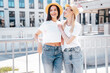 Two young beautiful smiling hipster female in trendy summer white t-shirt and jeans clothes. Carefree women posing in the street. Positive models having fun outdoors. Cheerful and happy. In hat