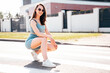 Young beautiful smiling female in trendy summer blue cycling shorts and tank top clothes. Carefree woman posing in street. Positive model having fun. Cheerful and happy. In sunglasses. Sits on asphalt