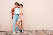 Young smiling beautiful woman and her handsome boyfriend in casual summer clothes. Happy cheerful family. Female having fun. Couple posing in street at sunny day. Near  wall. Having tender moments