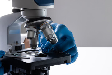 Poster - Close up of hand in glove using laboratory microscope and copy space on white background