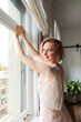 © Rafa Fernandez - Romantic lady, red hair woman in white vintage dress stands next to window.