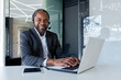 © Liubomir - Portrait of african american businessman inside office at workplace, mature man using headset phone and laptop for remote consultation with clients, smiling and looking at camera.