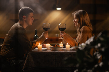 Wall Mural - Trough window view on young couple in love drinking wine, celebrating Valentines day dining at home, having romantic dinner date with candles