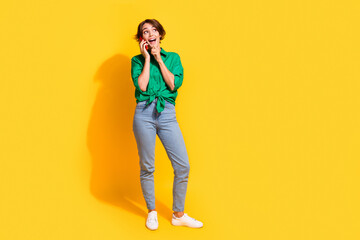 Wall Mural - Full length photo of excited impressed lady wear green shirt communicating modern gadget looking empty space isolated yellow color background