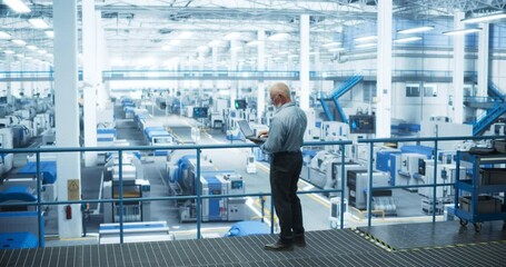Fototapete - Experienced Male Engineer Standing on a Platform, Using Laptop Computer and Overlooking Production at a Modern Automated Electronics Manufacture with AI Support. Factory Executive at Work