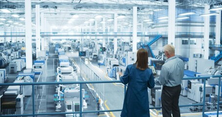 Aufkleber - Male Engineer and Female Project Manager Standing on a Platform, Talking, Using Laptop Computer and Monitoring Production at a Modern Automated Electronics Manufacture with AI Robotic Arms