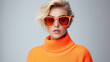 © Santy Hong - Fashionable confident blonde woman wearing trendy orange sweatshirt, color sunglasses, posing on white background.