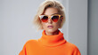 © Santy Hong - Fashionable confident blonde woman wearing trendy orange sweatshirt, color sunglasses, posing on white background.
