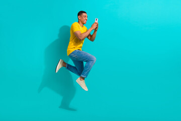 Canvas Print - Full length profile portrait of excited handsome guy jump rush use smart phone empty space isolated on turquoise color background