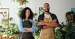Portrait of African American joyful couple happy man and woman in aprons standing at own small flower shop and looking smiling to camera. Family business concept.