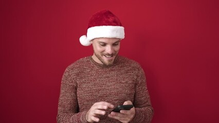 Poster - Young caucasian man using smartphone with winner expression wearing christmas hat over isolated red background