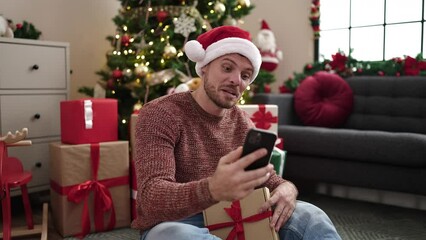 Wall Mural - Young caucasian man showing gift on a video call with smartphone at home