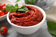 Tasty tomato paste and basil in bowl on light gray table, closeup