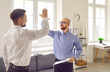 Two business people make a successful, good, profitable deal. Two happy young men standing in the office, smiling and giving each other a high five. Cooperation, teamwork, partnership, success concept
