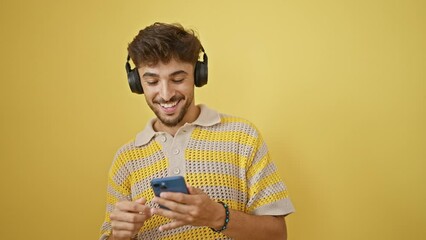 Canvas Print - Cool arab man confidently listening and dancing to upbeat music on his smartphone, creating an isolated yellow background of happiness and positivity