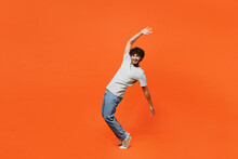 Full Body Side View Young Smiling Happy Indian Man He Wears T-shirt Casual Clothes Stand On Toes Leaning Back With Outstretched Hands Isolated On Orange Red Color Background Studio. Lifestyle Concept.