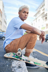 Skateboard, street style and city with a black man on the sidewalk in the day for skating, sport or leisure. Skater, recreation and urban with a cool or edgy male sitting on a pavement with his board