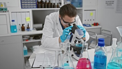 Wall Mural - Young hispanic man scientist writing report using microscope at laboratory