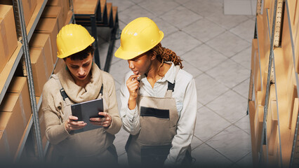 Wall Mural - Diverse women planning order shipment with tablet, looking at cardboard packages on storage room racks. Supervisor and employee checking merchandise and products. Handheld shot.