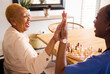 Black people, nurse and high five in elderly care for chess, fun or social activity or game together at home. African medical professional touching hands with senior female person with a disability
