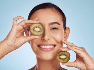 Wall Mural - Skincare, kiwi and woman with face or eye beauty, cosmetics and natural product, health and vitamin c. Portrait of young happy person or model, green fruits and dermatology on studio, blue background