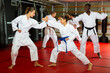 © JackF - Women and man in white kimono standing in fight stance and sparring during group karate training. Their trainer, African-american man, standing beside and watching.