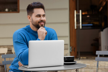 Poster - Handsome young man with laptop at table in outdoor cafe. Space for text