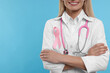 Doctor with pink ribbon and stethoscope on light blue background, closeup and space for text. Breast cancer awareness