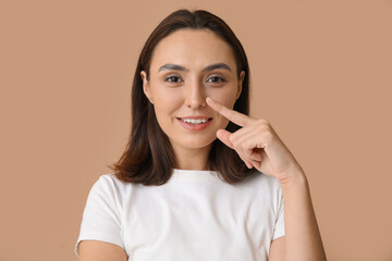 Sticker - young woman pointing at her nose on beige background, closeup