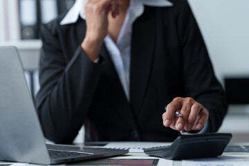 Wall Mural - Asian businesswoman works on laptop and calculates with financial calculator from graphs, statistics, charts. Planning. Business success results in modern office.