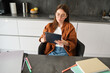 E-learning and remote education concept. Young woman in glasses, works from home in kitchen, looking at digital tablet, connects to online class or course