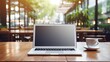 © DigitalArt - A serene workspace setup with a laptop on a wooden table beside a steaming cup of coffee. The backdrop showcases a café ambience with hanging lights and verdant plants, mockup