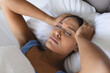 © Wavebreak Media - Sick biracial woman wearing blue pyjamas touching her head in bedroom