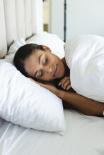 Happy Biracial Woman Sleeping On White Pillows In Bedroom