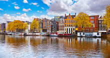Amsterdam, Netherlands. Panoramic View Of Channels In Amsterdam City. Dancing Houses. River Amstel. Old European Landmark. City Autumn Fall Landscape With Blue Sky Clouds