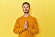 © Asier - Young Caucasian man on a yellow studio background praying, showing devotion, religious person looking for divine inspiration.