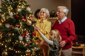 Wall Mural - Grandparents and granddaughter decorating christmas tree