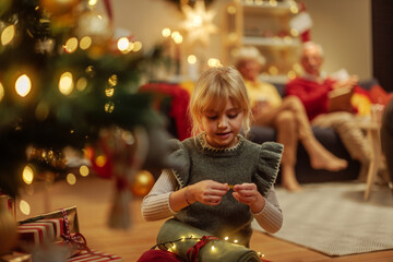 Wall Mural - Little girl packing Christmas present in front of a Christmas tree